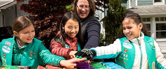 Three Girl Scouts and a volunteer hands in the middle at a cookie sale